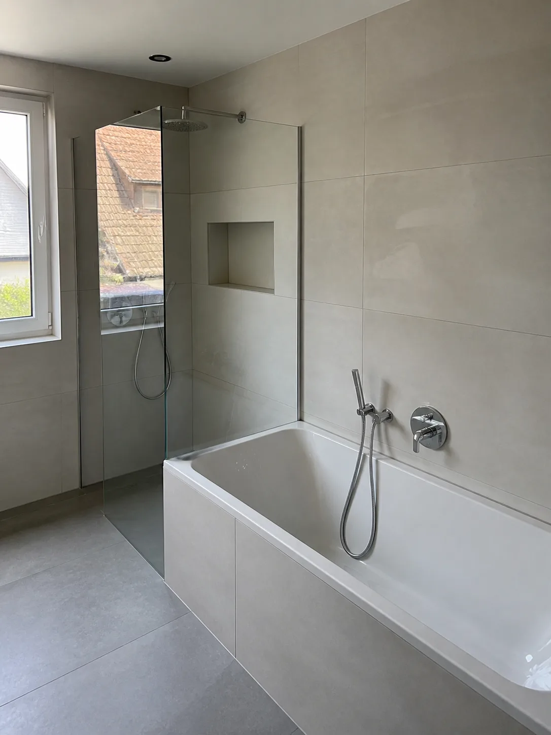 Modernisiertes Bad mit Badewanne, bodengleicher Dusche und großformatigen Fliesen.