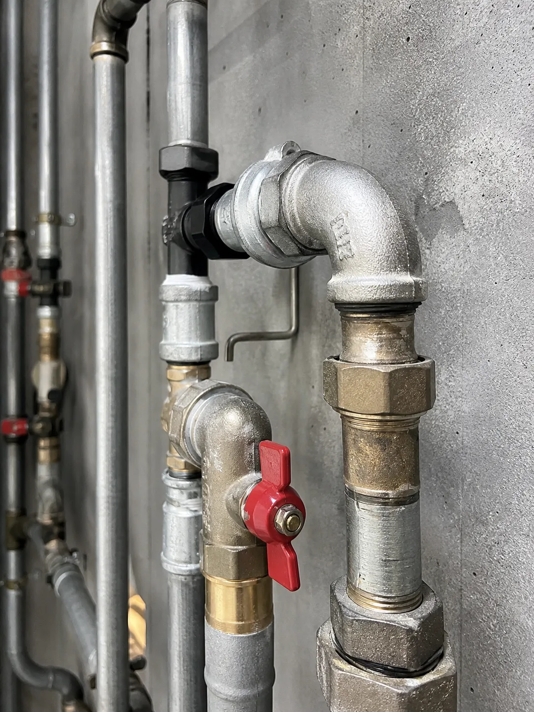 Installierte Versorgungsleitungen mit Formstücken und Absperrventilen vor einer Betonwand.