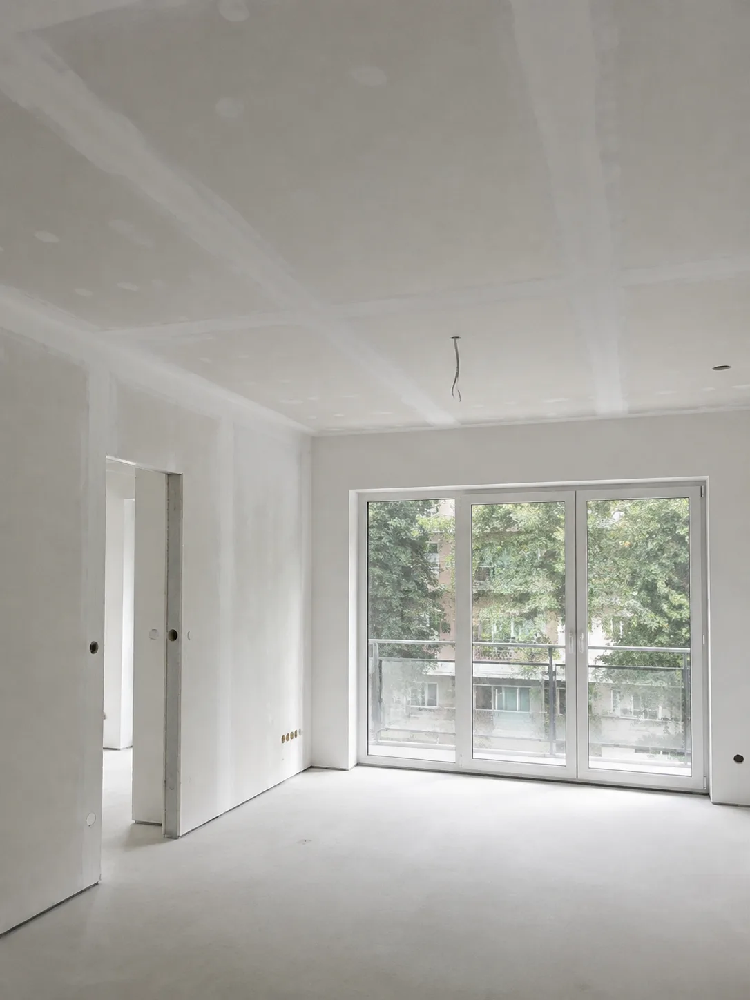 Heller Innenraum mit vorbereiteten Wand- und Deckenflächen und großen Fenstern.